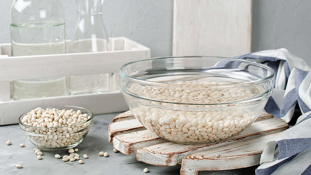 Weiße Bohnen quellen in einer Schüssel mit Wasser, daneben eine kleine Schale mit getrockneten weißen Bohnen