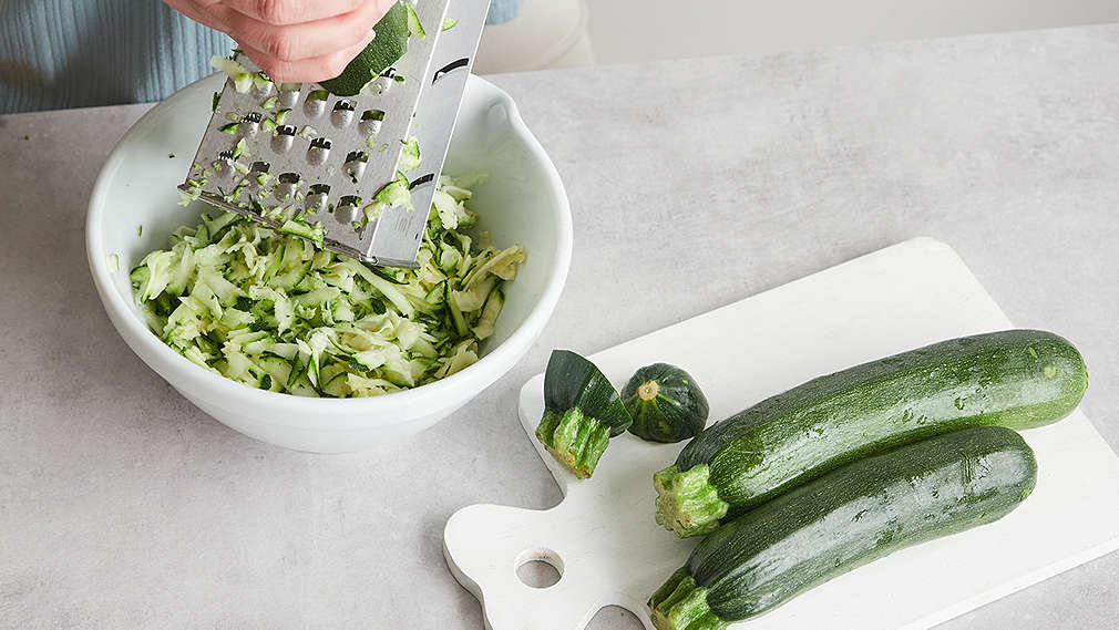 Frische Zucchini wird mit einer Handreibe grob gerieben