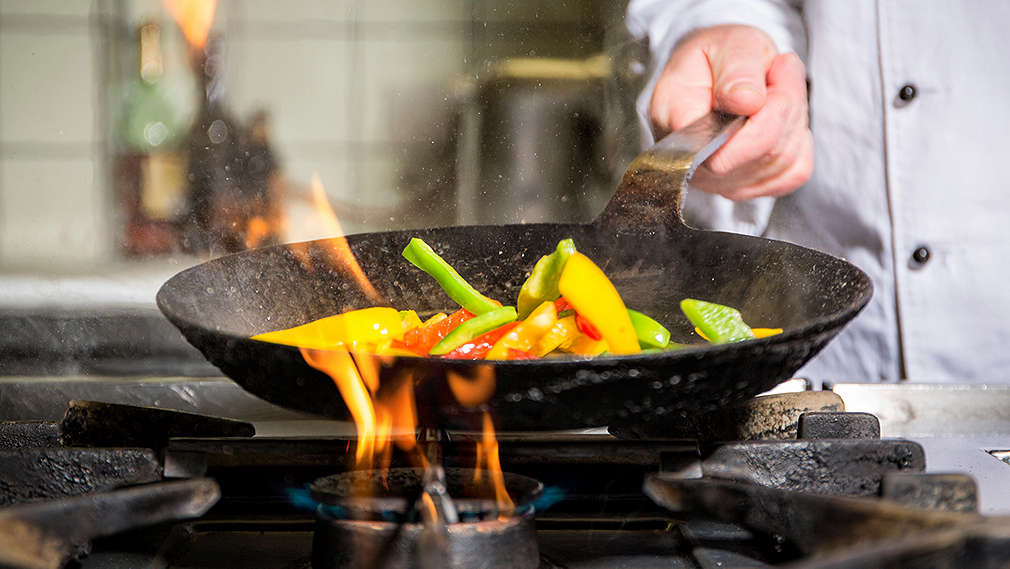 Gemüse wird in einer Wok-Pfanne auf einem Gasherd sautiert