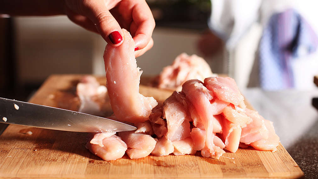 Hühnchenfleisch wird auf einem Holzschneidebrett in Streifen geschnitten
