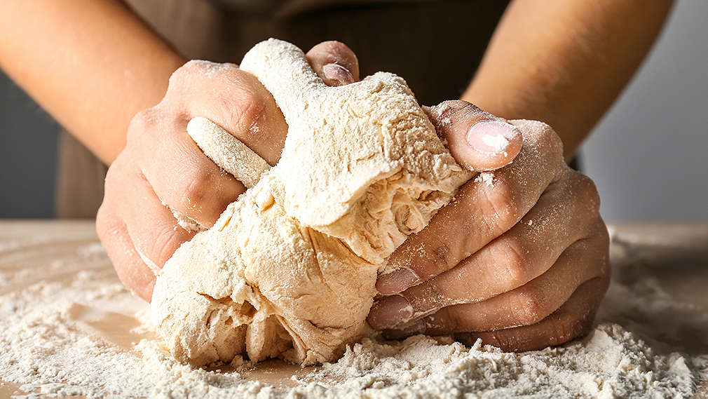 Person knetet Teig auf einer Arbeitsfläche, die mit Mehl bestäubt ist