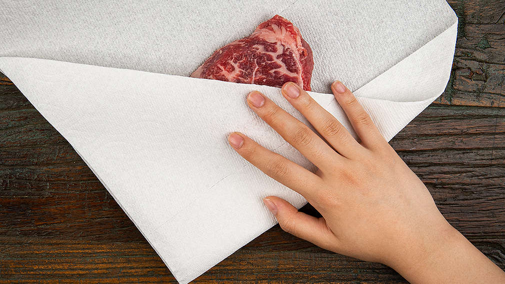 Ein Stück Fleisch wird mit Küchenpapier trocken getupft