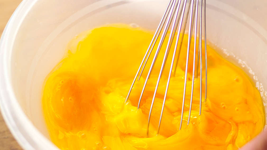 Mehrere Eigelbe werden mit einem Handschneebesen in einer Schale verquirlt