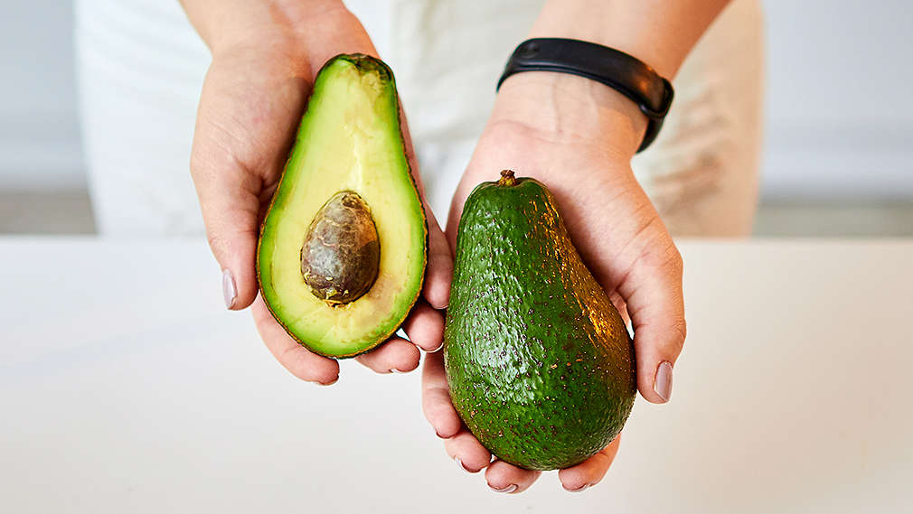 Zwei Hände im Anschnitt zeigen eine halbe und eine ganze Avocado