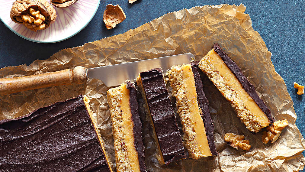 Ein Kuchen mit Schokoladenglasur, der ohne Mehl gebacken wurde, liegt auf dem Tisch auf einem Stück backpapier, daneben ein Schälchen mit Walnüssen