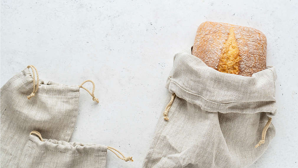 Ein Ciabatta-Brot liegt in einem Leinen-Brotbeutel auf hellgrauem Grund