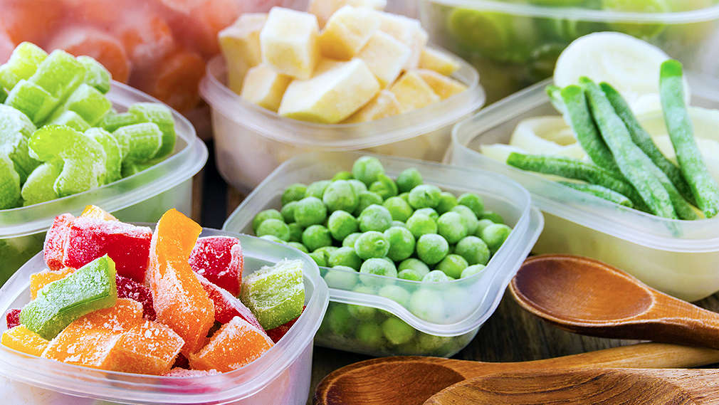 Mehrere Aufbewahrungsdosen mit gefrorenen Gemüsesorten, besonders prägnant im Vordergrund sind unterschiedliche Sorten Paprika sowie Erbsen, Bohnen und Sellerie zu sehen