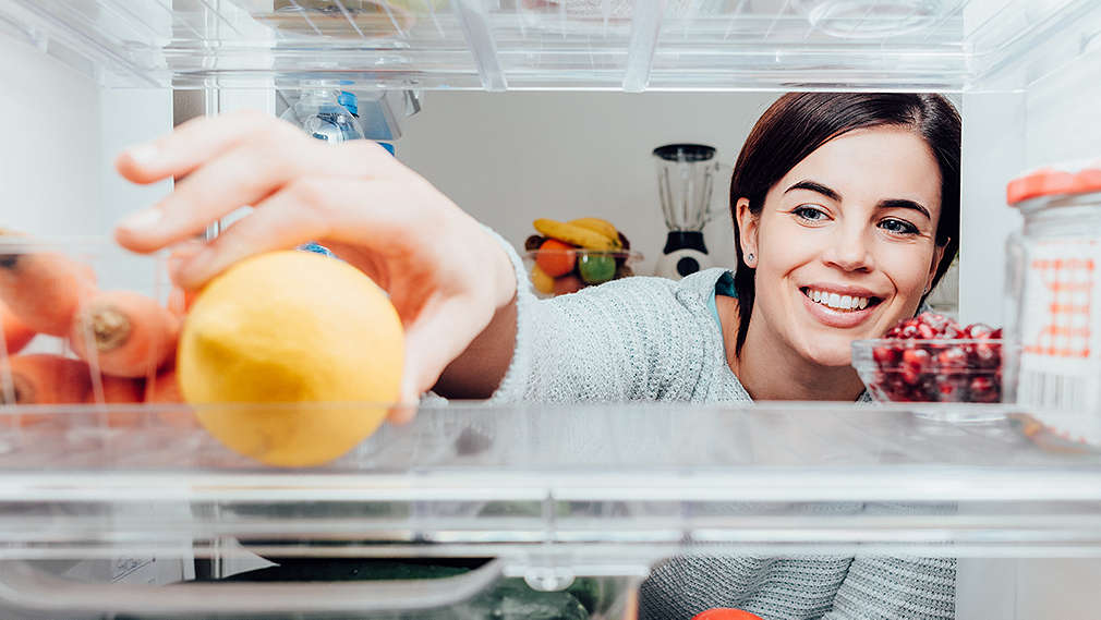 Frau greift nach Zitrone im Kühlschrank