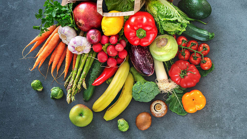 Abbildung von Obst und Gemüse auf einem dunkelgrauen Hintergrund.