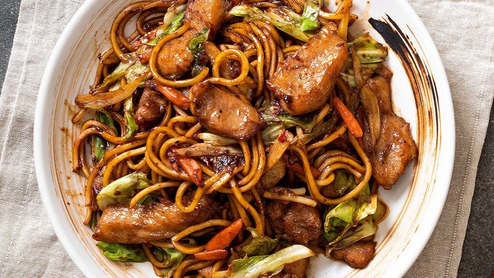 Zu sehen sind gebratene Asia-Nudeln in einem weißen tiefen Teller