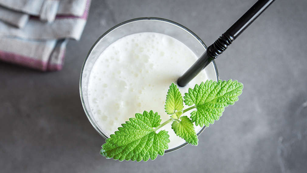 Ein Glas Ayran mit Minze und Strohhalm auf dunklem Untergrund