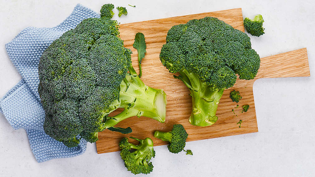 Zwei Brokkoli-Köpfe liegen auf einem Holzschneidebrett