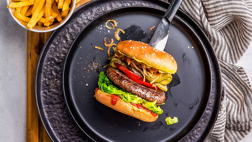 Burger von oben auf einem schwarzen Teller fotografiert, daneben eine kleine Schale mit Pommes