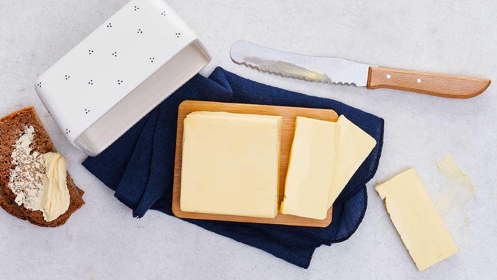 Ein Stück angeschnittene Butter in einer weißen Butterbox, daneben ein Buttermesser