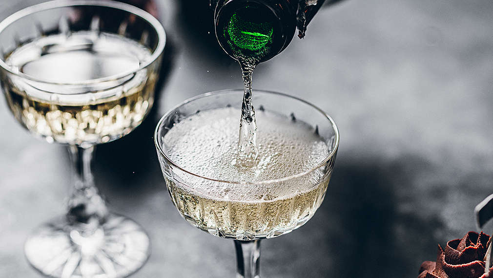 Zu sehen sind zwei Champagnergläser auf dunklem Untergrund