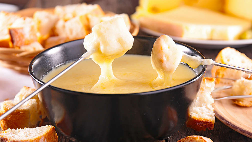 Brotwürfel werden auf einer Fonduegabel in ein Käsefondue getunkt