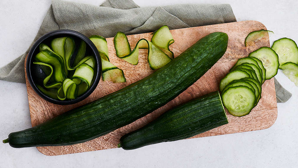 Frische Gurke im Ganzen, geschnitten und gehobelt auf einem Holzschneidebrett angerichtet