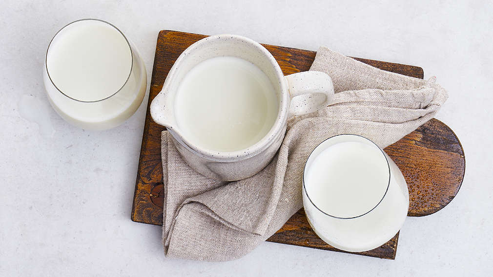 Ein Krug und zwei Gläser mit Hafermilch auf einem Holzbrett