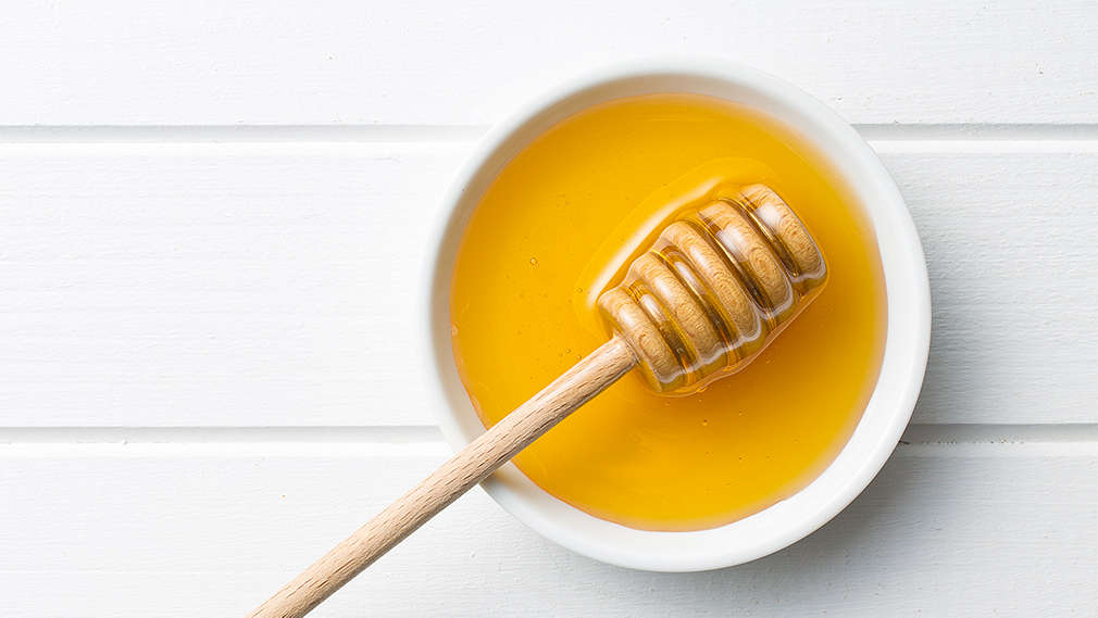 Flüssiger Honig in einem weißen Schälchen mit Honiglöffel aus Holz