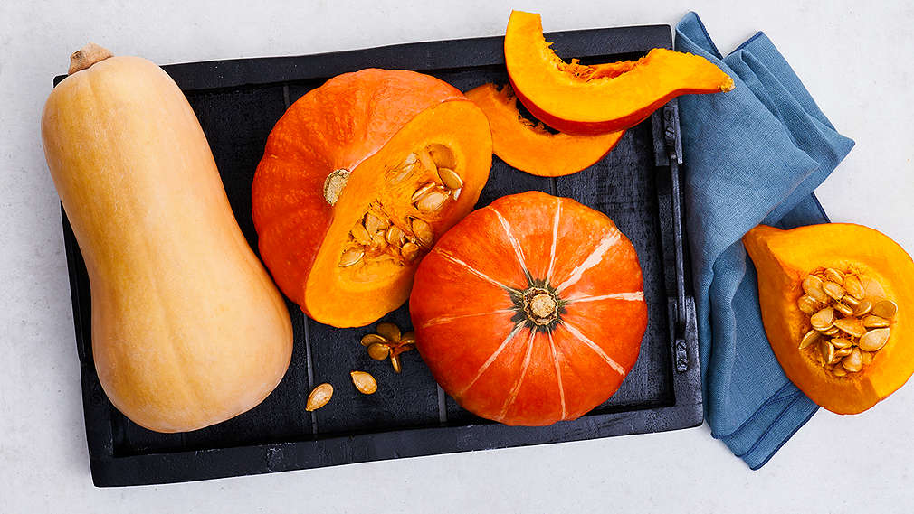 Zwei ganze Kürbisse und ein Kürbis in mehrere Teile geschnitten liegen auf einem schwarzen Tablett.