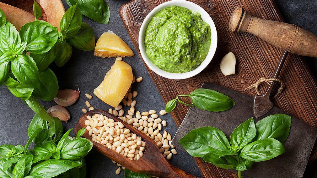 Schälchen Pesto, Basilikum, Knoblauch, Käse und Nüsse auf einem dunklen Holzbrettchen