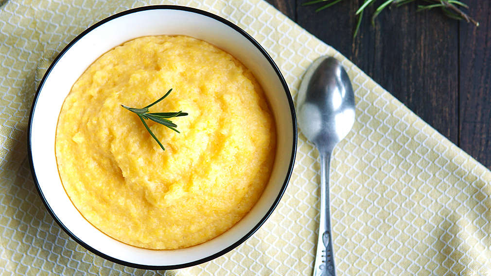 Polenta dekoriert mit einem kleinen Rosmarinzweig in einer weißen Schale auf einem Esstisch