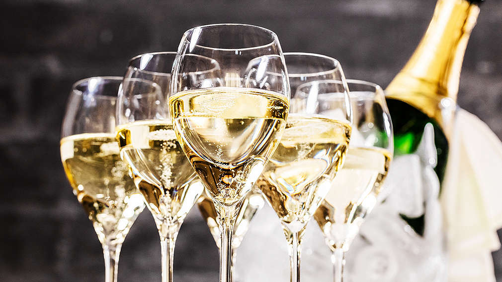 Mehrere Gläser Sekt mit einer Flasche Sekt im Kühler im Hintergrund