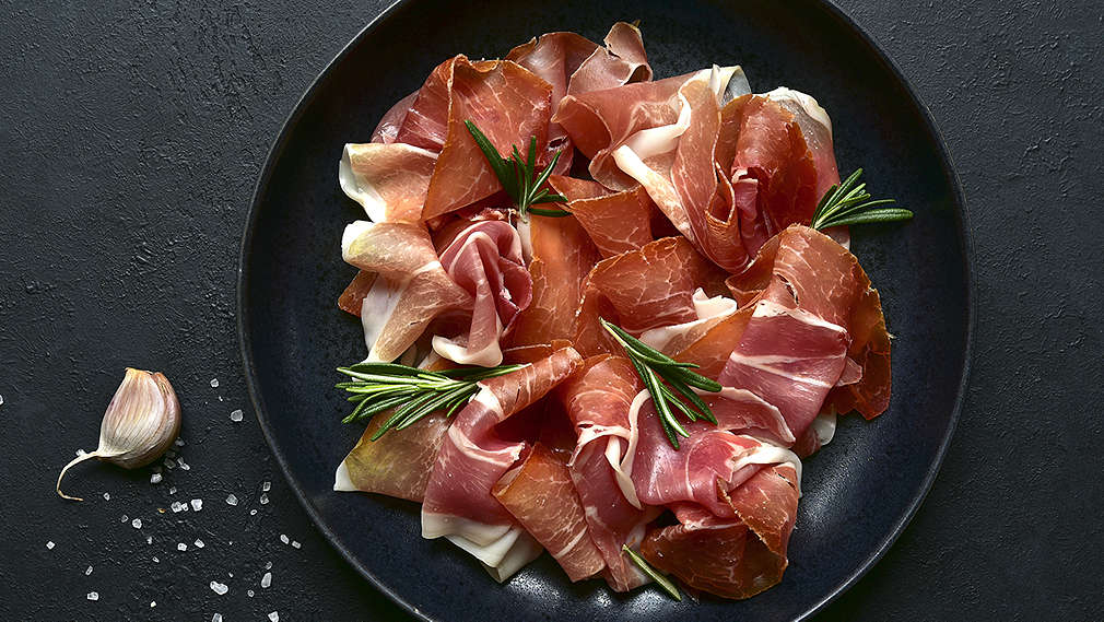 Serranoschinken mit Kräutern auf einem schwarzen Teller angerichtet