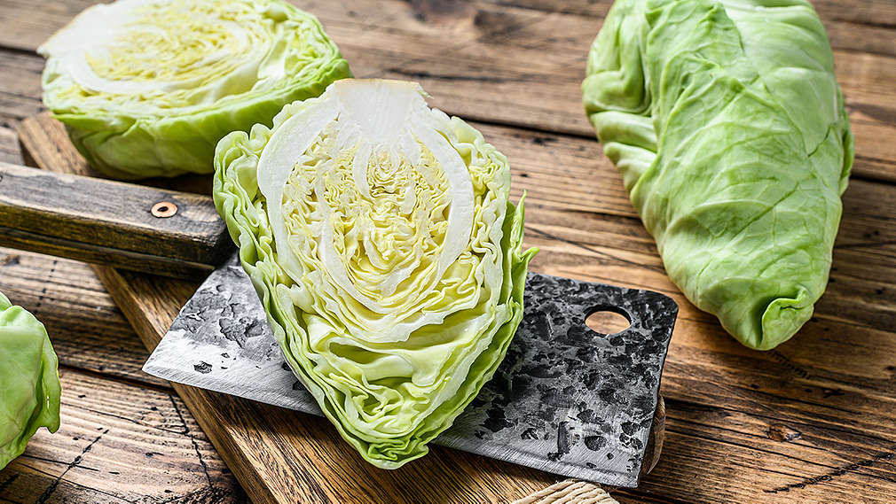 Ein ganzer und ein halbierter Spitzkohl liegen neben einem Messer auf einem Holzbrett