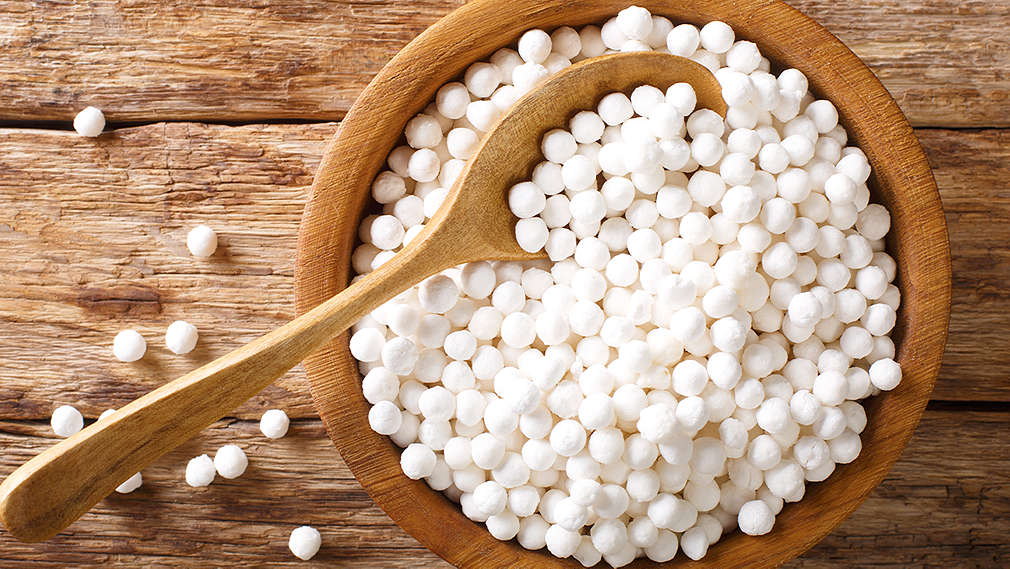Eine Holzschale mit weißen Tapioka-Kugeln und einem Holzlöffel darin steht auf einem Holztisch