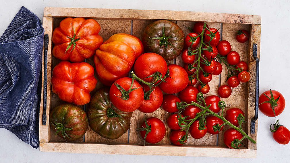 Tomaten in unterschiedlichen Größen und Sorten liegen in einem Servier-Tablett aus Holz