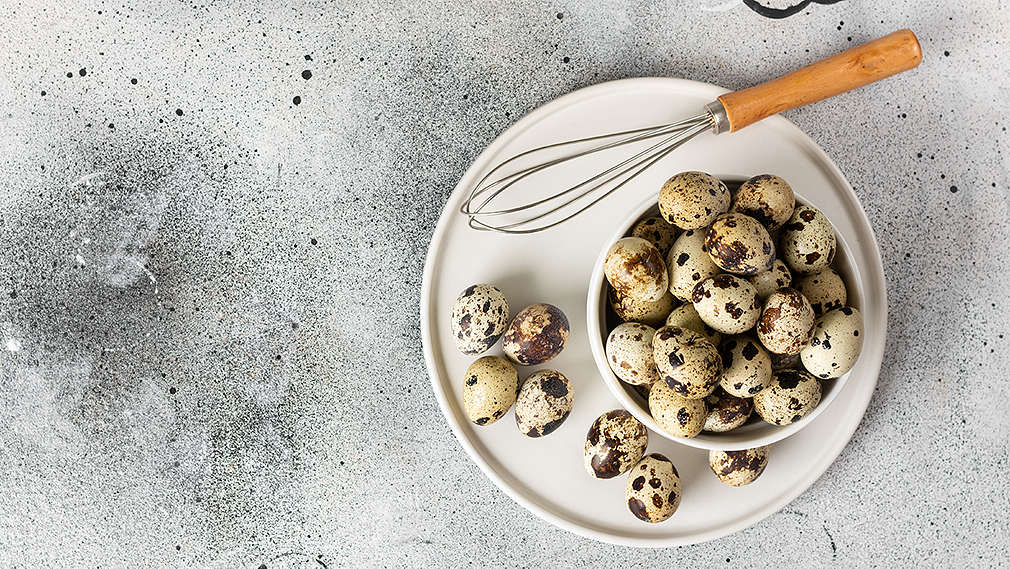 Eine Schüssel mit Wachteleiern, daneben liegt ein Schneebesen 