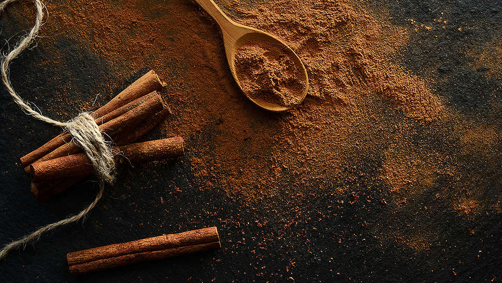 Gemahlener Zimt und Zimtstangen auf schwarzem Grund