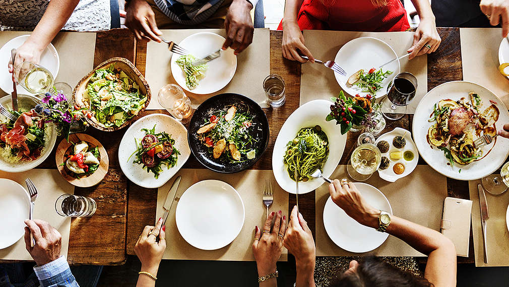 Изображение на хора, които похапват на маса, отрупана с храна