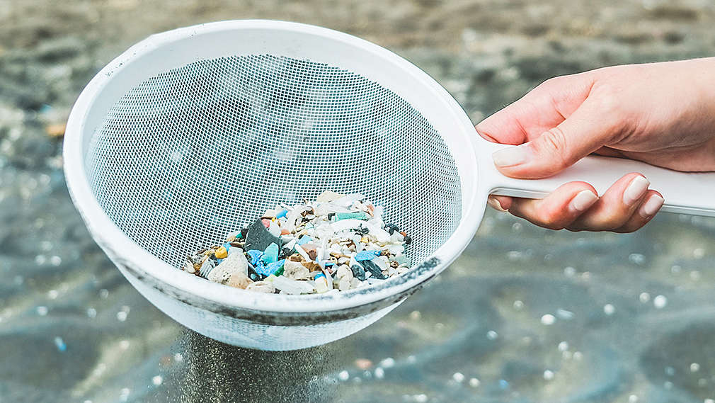 Ruka držící podběrák s malými kamínky a kousky mikroplastů.