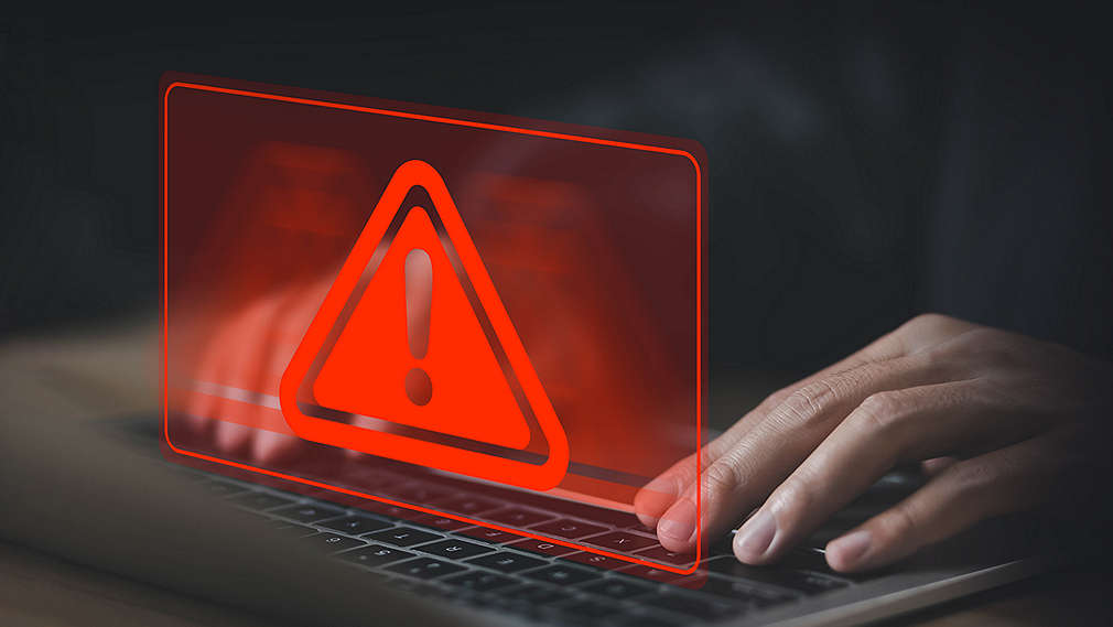 Ruce na klávesnici notebooku a symbol červeného vykřičníku