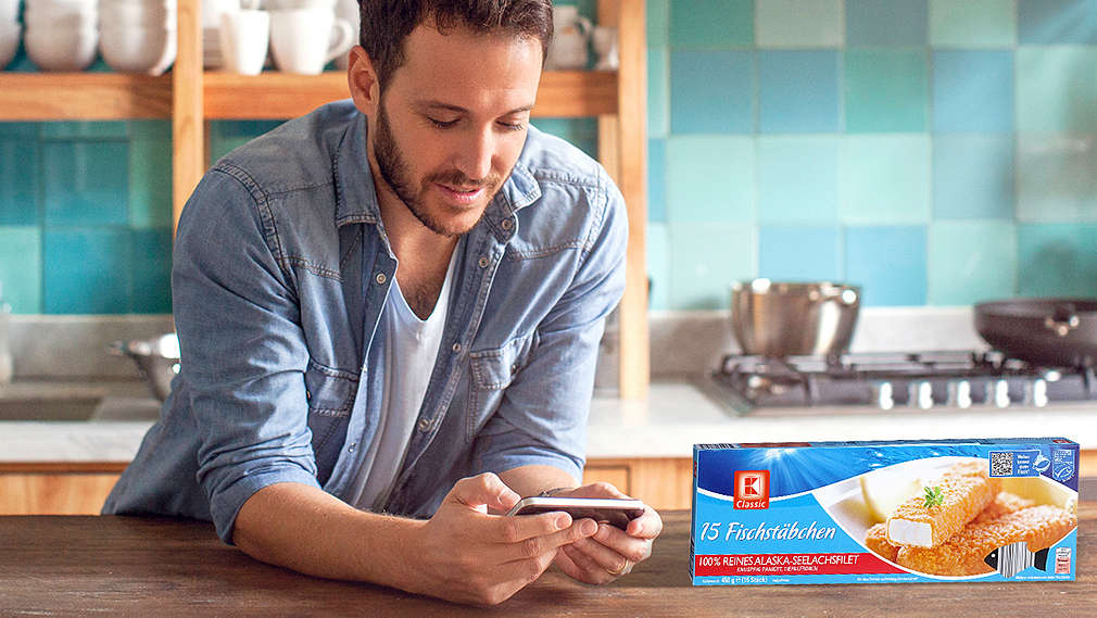 Мъж с мобилен телефон и опаковка рибни филенца нa K-Classic