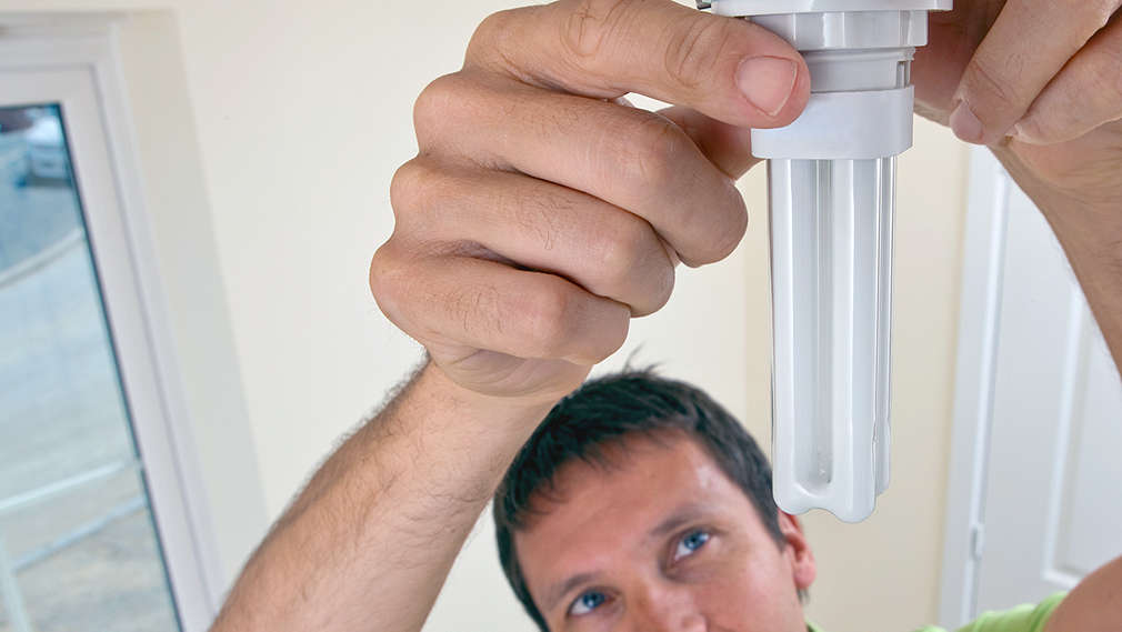 Mann wechselt Energiesparlampe aus