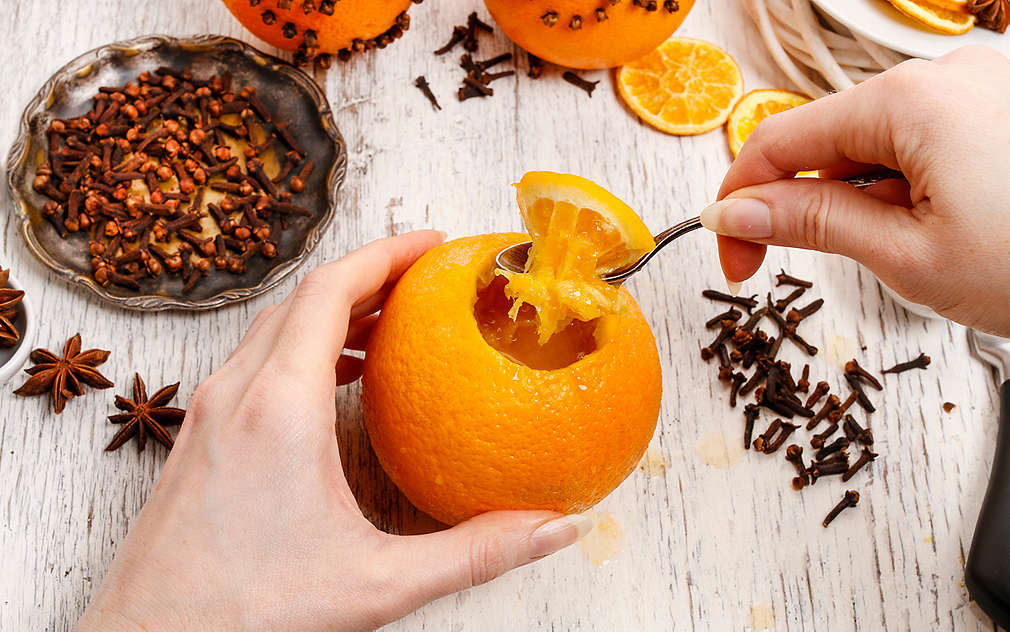 O portocală fotografiată de sus; se pot vedea două mâini de femeie care scot o bucată rotundă din portocală cu o linguriță.