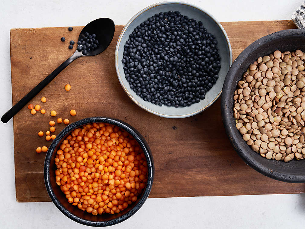 Diverse sortimente de linte proaspătă în boluri pe un tocător din lemn, în stânga, pe tocător, se află o lingură neagră