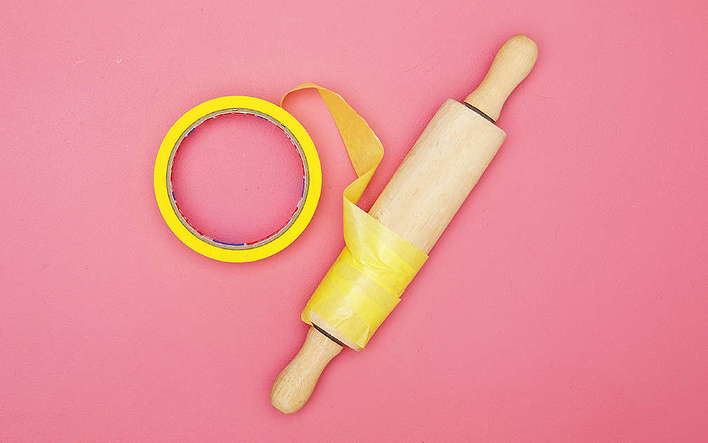 Na różowym tle widać wałek do ciasta owinięty dwustronną taśmą klejącą.