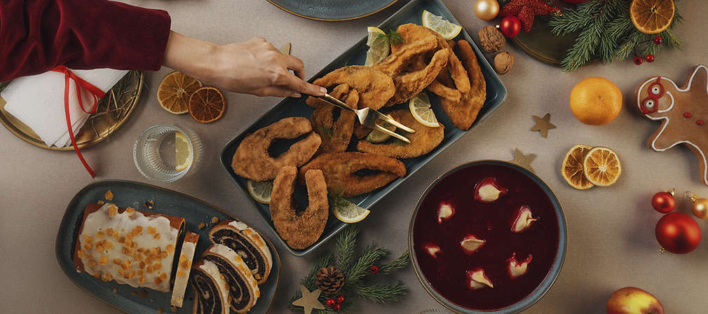 Stół świąteczny z widocznymi półmiskami z dzwonkami karpia, makowcem i barszczem z uszkami